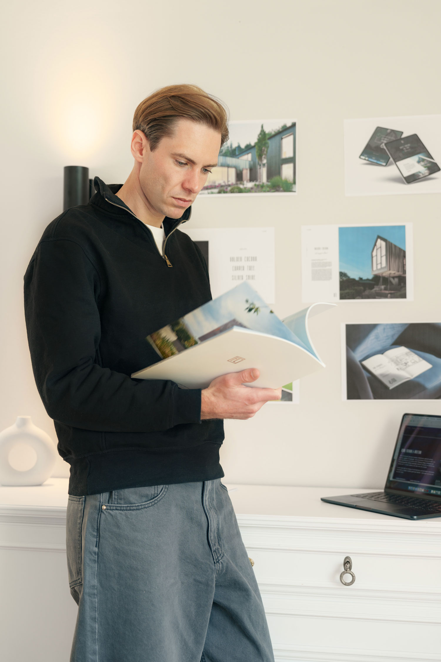 Mann betrachtet Designmagazin im Büro vor Wand mit Projekten