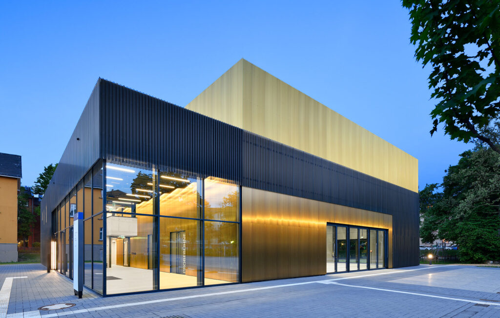 Modernes Gebäude mit goldfarbener Metallfassade und großen Glasflächen, beleuchtet bei Dämmerung