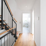 Moderne Treppe und Flur im Obergeschoss einer Doppelhaushälfte in Aystetten bei Augsburg mit Holzstufen und schwarzem Geländer